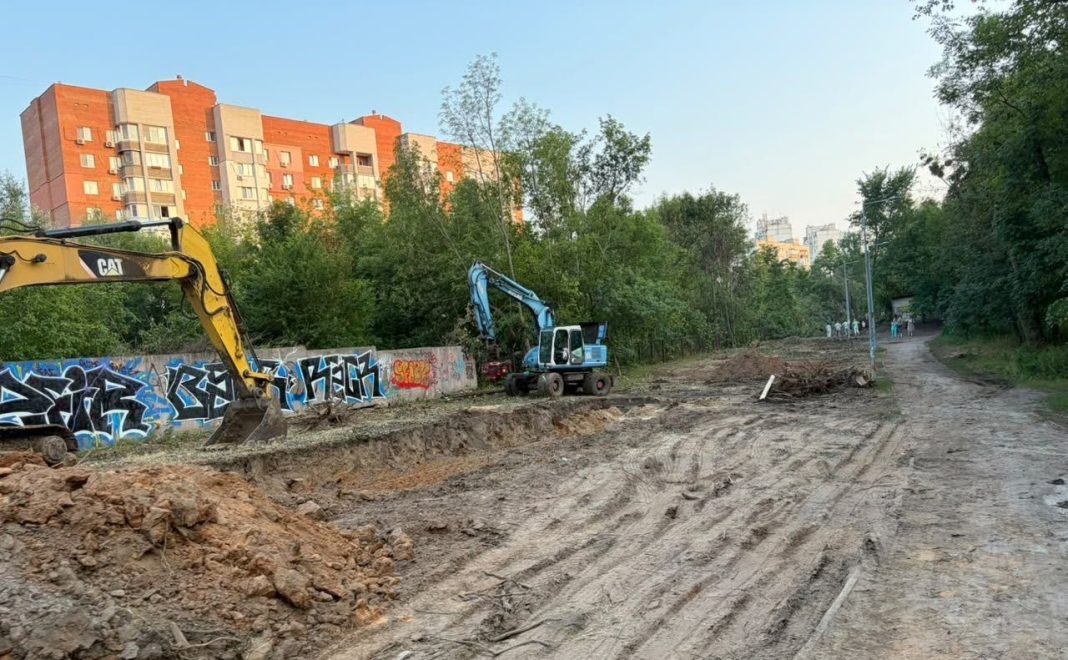 Екскаватори працюють на ділянці серед дерев біля житлових будинків