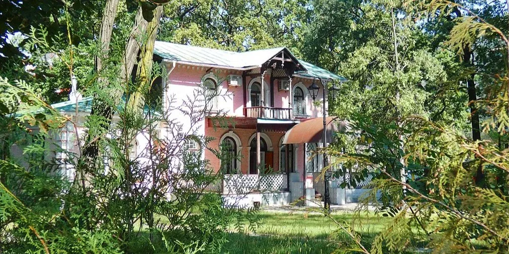 Будівля «Дача з мезоніном» у Києві взимку — історичний особняк із рожевим фасадом, зеленим дахом, дерев’яним балконом і засніженою територією.